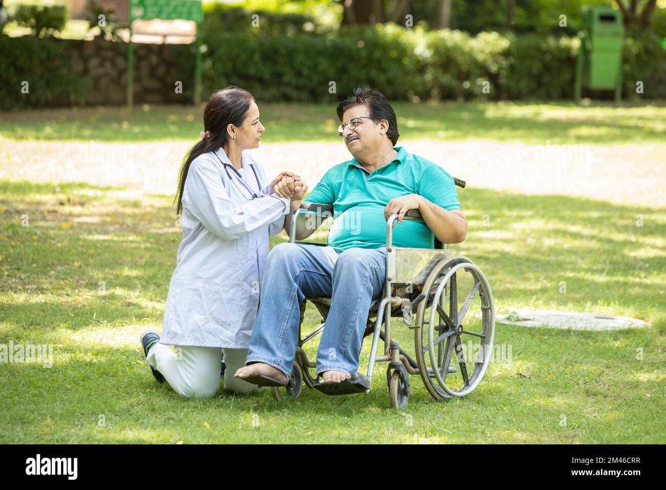 Indian caregiver nurse taking care of senior male patient in a wheelchair outdoor at park, Asian doctor help and support elderly mature older people. Stock Photo