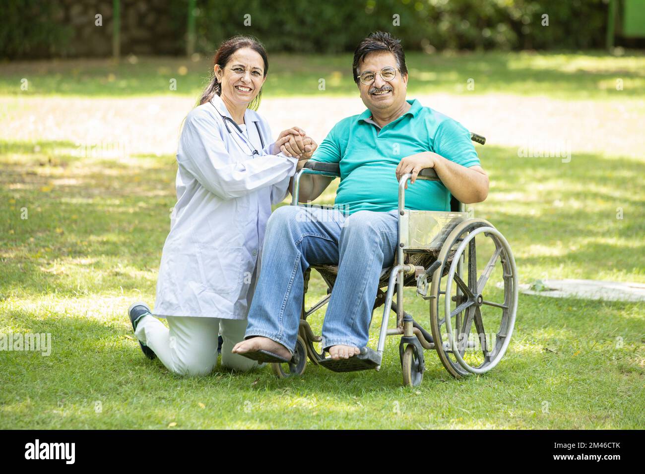 Happy Indian caregiver nurse taking care of senior male patient in a wheelchair outdoor at park, Asian doctor help and support elderly mature older pe Stock Photo