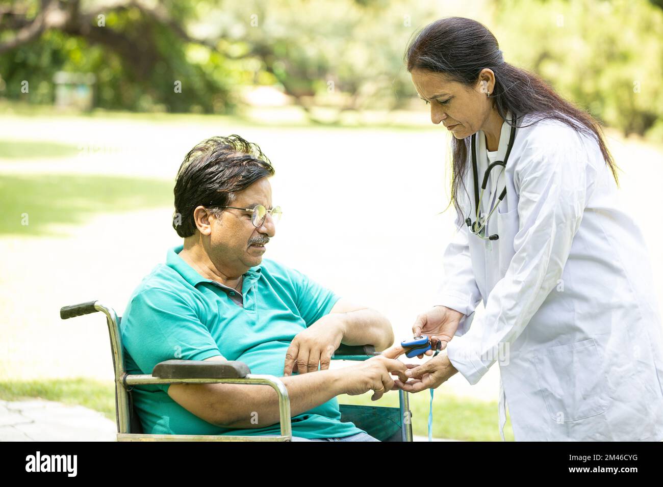 Indian doctor check with pulse oximeter device on finger of senior male diabetes patient in a wheelchair outdoor at park. Stock Photo
