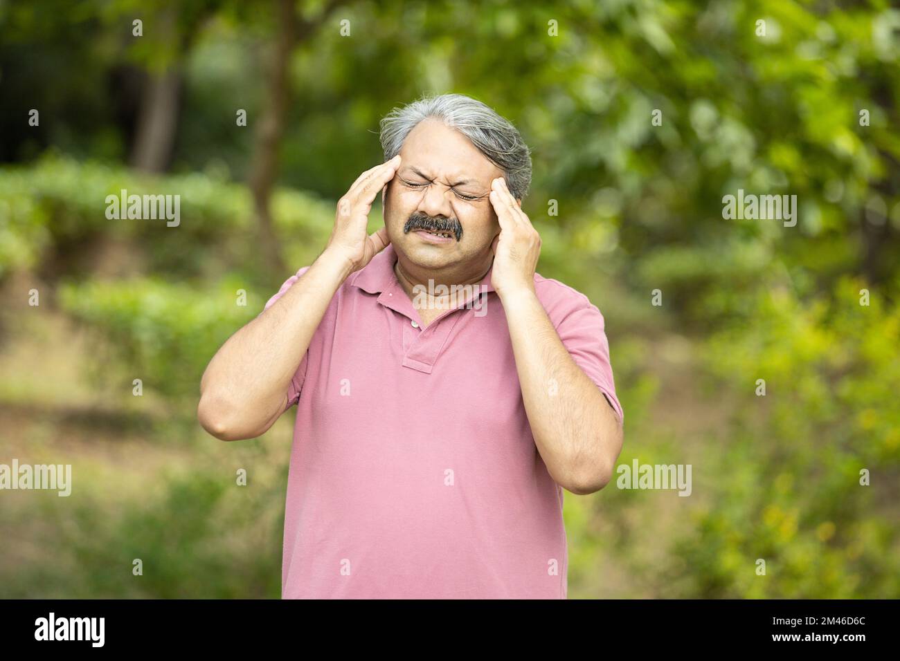 Indian senior man suffering from headache standing outdoor at park. Stressed old people, Stock Photo