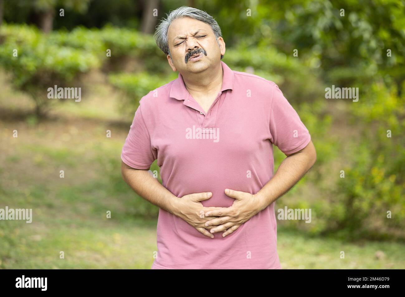 Indian senior man having stomachache or diarrhea outdoor at park, Asian Old male suffering from abdominal pain, health problem. Stock Photo