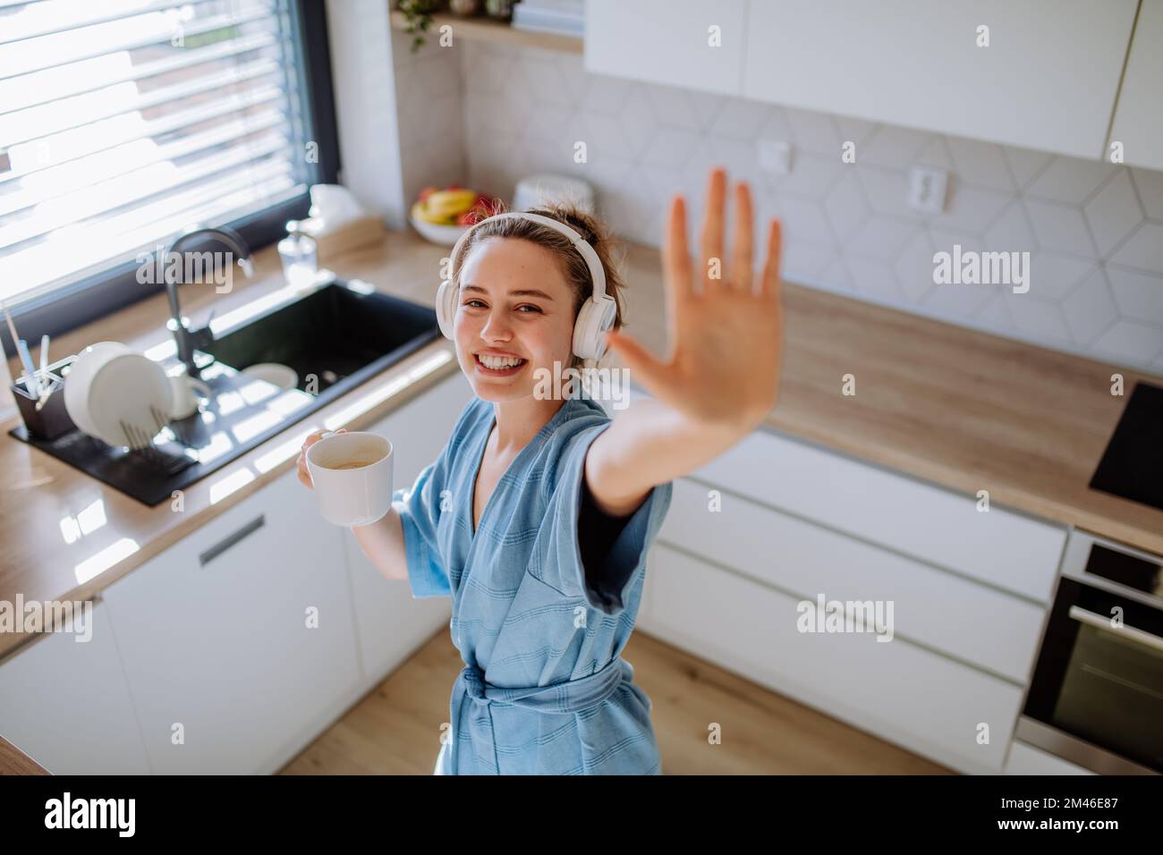 Young woman listening music and enjoying cup of coffee at morning, in her kitchen. Stock Photo