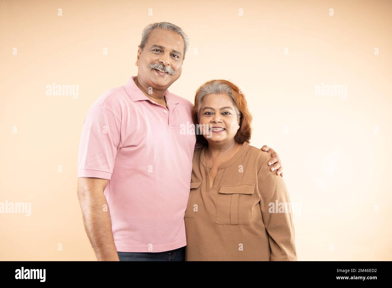 Portrait of Happy indian senior couple standing together over beige background. Old Asian man and woman smiling. Stock Photo