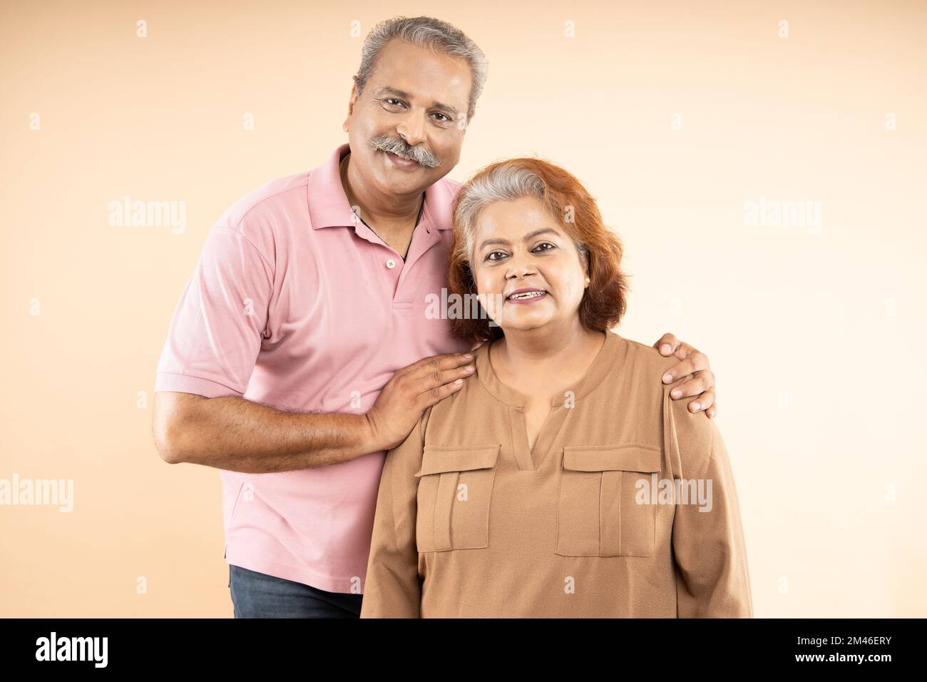 Portrait of Happy indian senior couple standing together over beige background. Old Asian man and woman smiling. Stock Photo