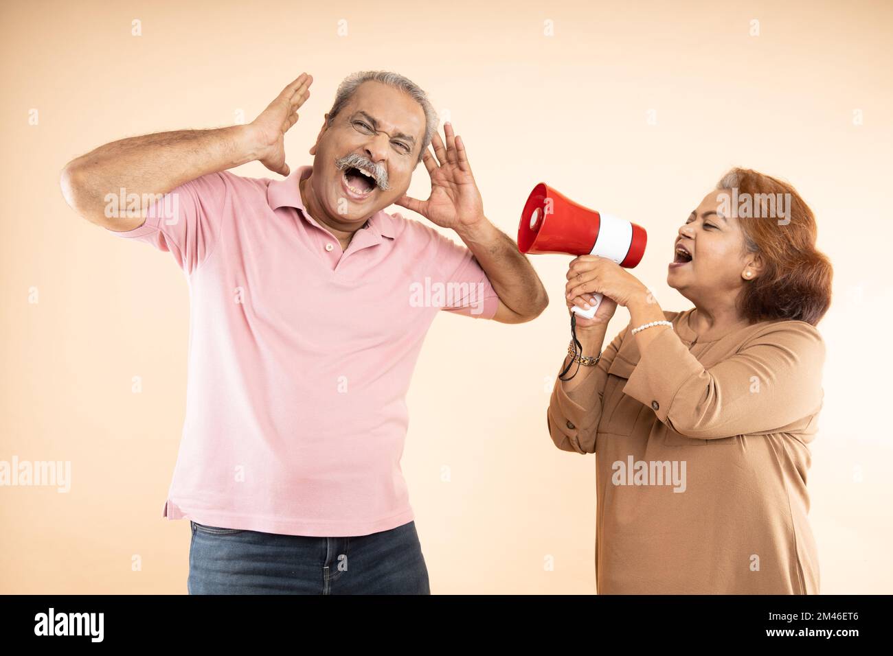 Senior indian woman scream or shouting at man in megaphone isolated on beige background. announce discounts sale. Asian wife tease husband. Stock Photo