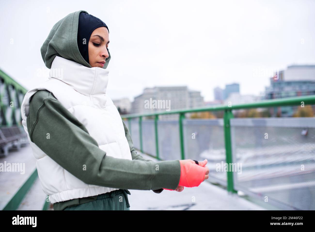 Young muslim woman putting on sports gloves, outdoor in a city Stock