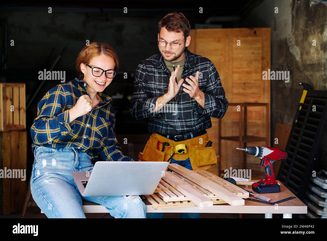 Woman and man celebrating teamwork success of their small business while working in their carpentry workshop. Stock Photo