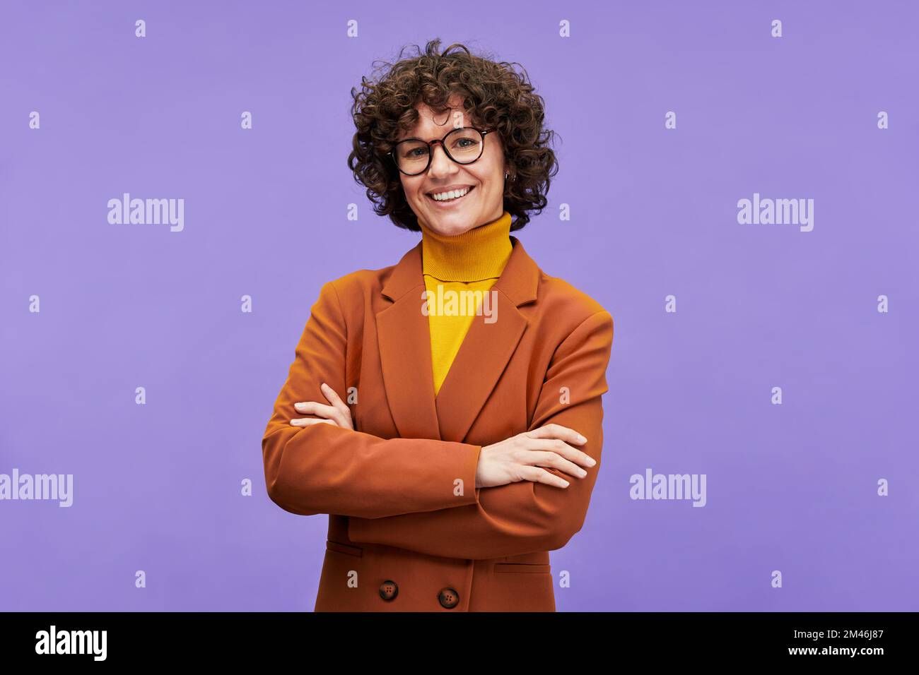 Happy brunette female employee or teacher in formalwear and eyeglasses crossing her arms on chest and looking at camera with smile Stock Photo