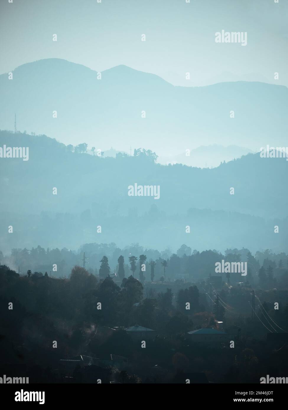 Layers of silhouettes of mountain ranges in fog, mist or smoke. Vertical banner nature landscape in blue color. Stock Photo
