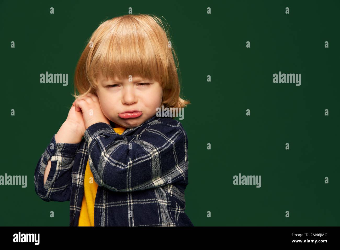 Portrait of cute little boy, child posing over green studio background. Feeling sleepy and tired. Acting up. Concept of childhood, emotions Stock Photo