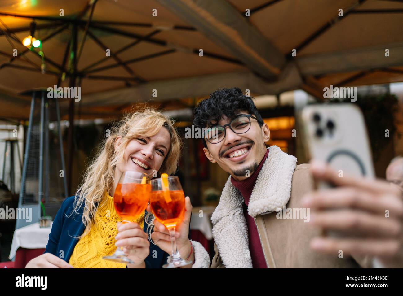 Young multi-ethnic smiling couple taking a selfie while sitting in a restaurant having a drink Stock Photo