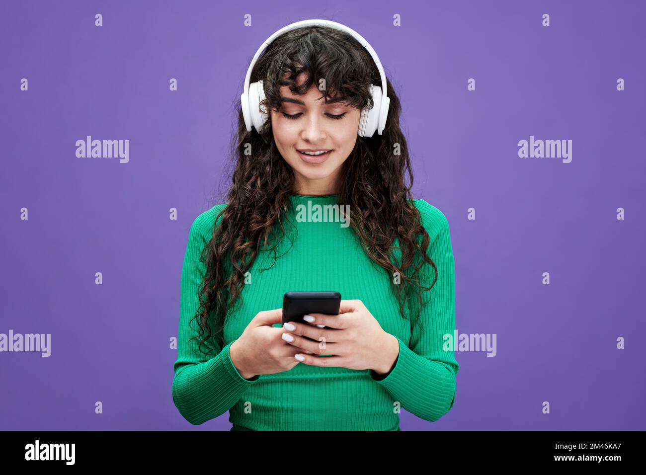 Pretty girl with dark long wavy hair scrolling through playlist in mobile phone and listening to her favorite music in headphones Stock Photo