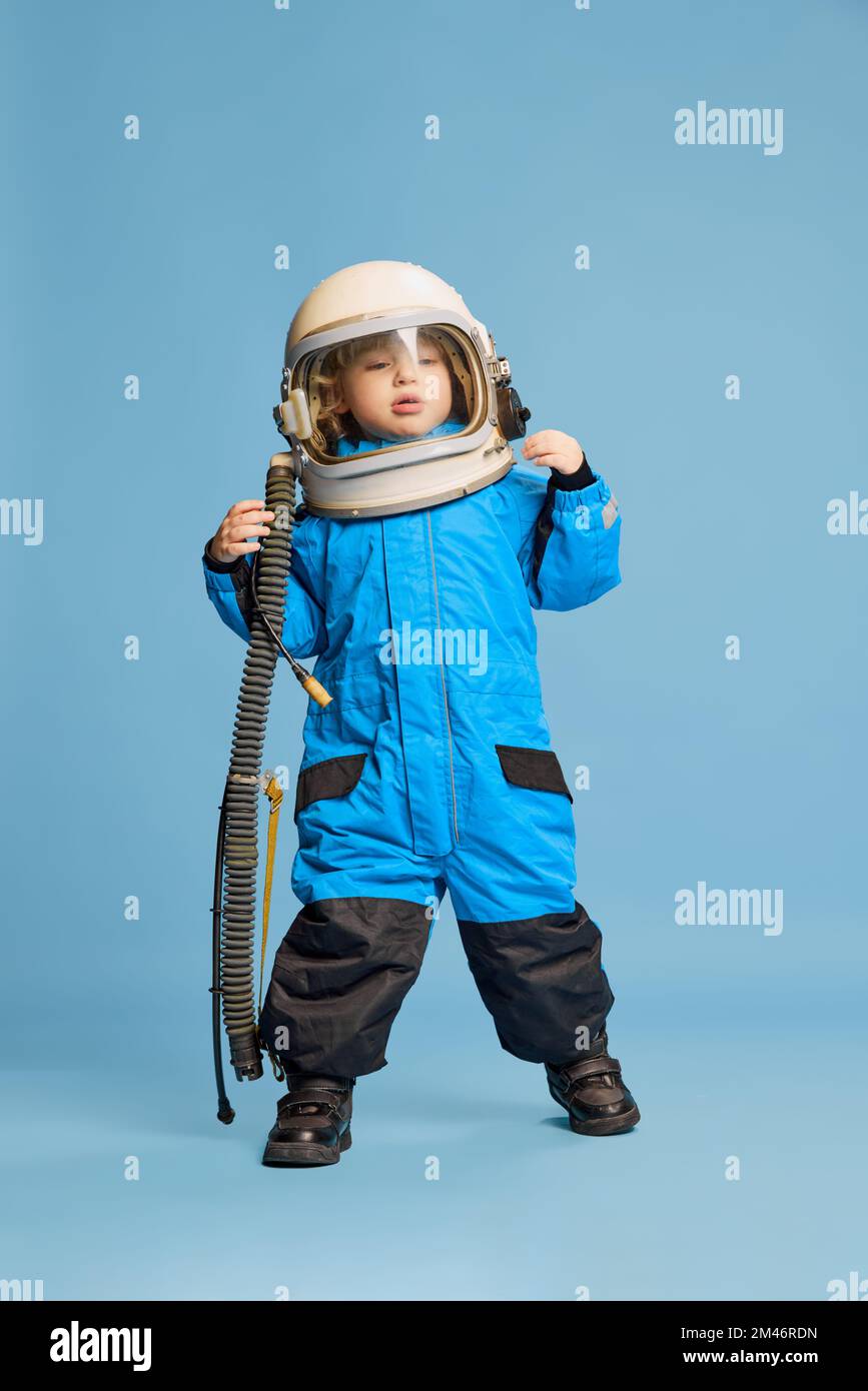 Portrait of little boy, child posing in astronaut costume over blue studio background. Playful kid, imagination. Concept of childhood, emotions Stock Photo