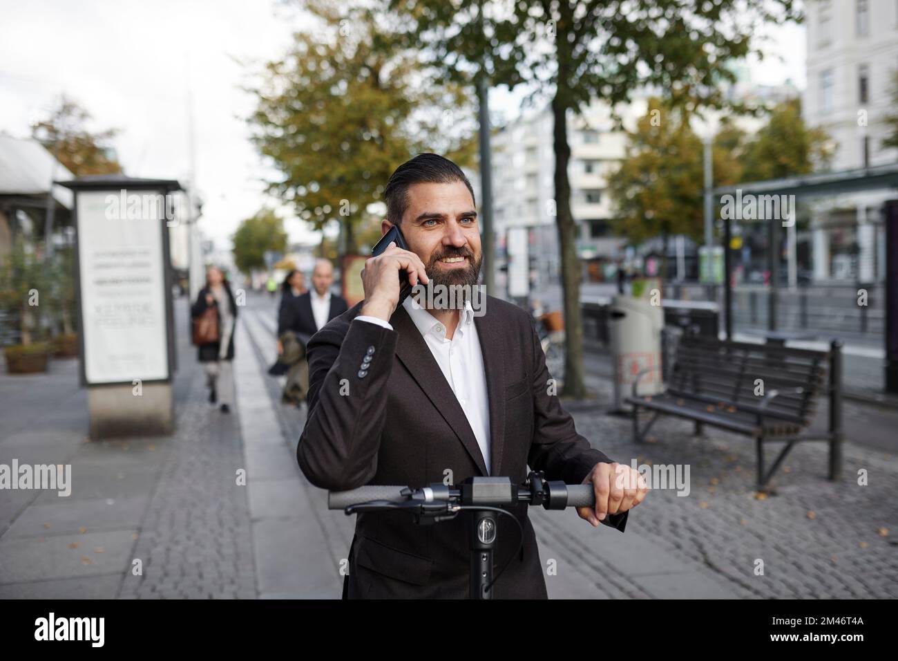 Businessman riding electric push scooter and talking on phone Stock Photo