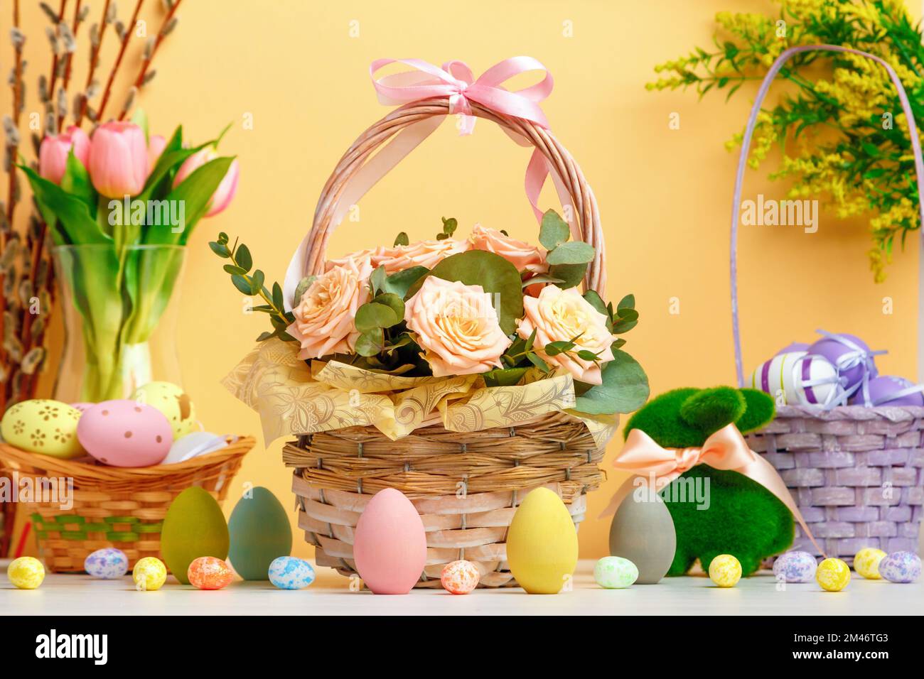 Easter composition. Basket with flowers and eggs toy rabbit on the table. Stock Photo