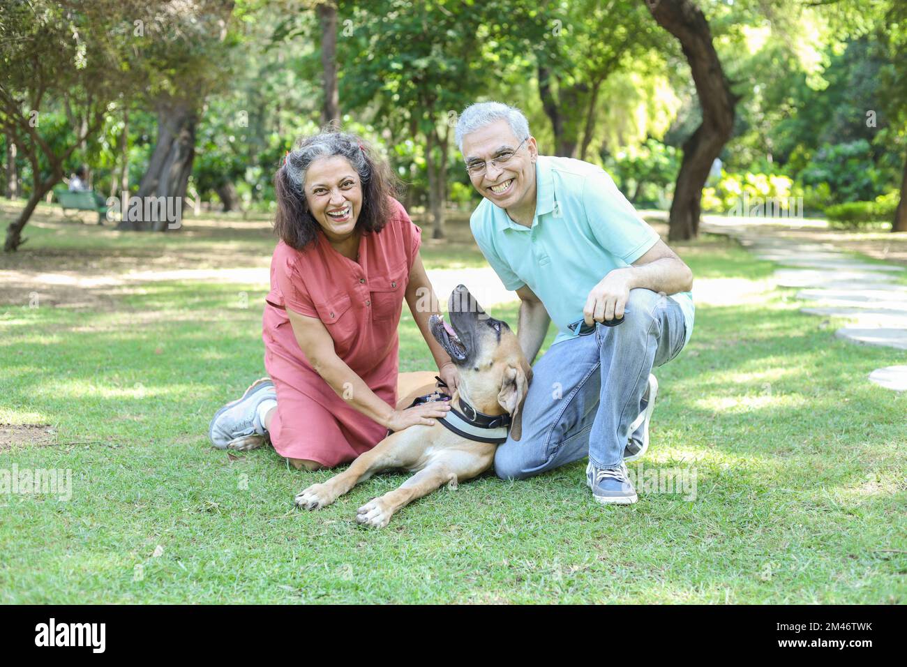 Happy indian senior couple playing with dog in summer park. Retirement life, retired people enjoying life in garden. having fun. Stock Photo