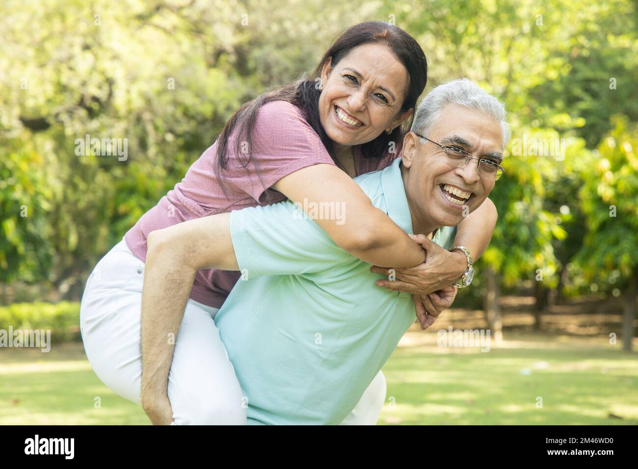 Happy indian senior couple enjoying life having fun at summer park, man giving piggyback ride to woman. Stock Photo