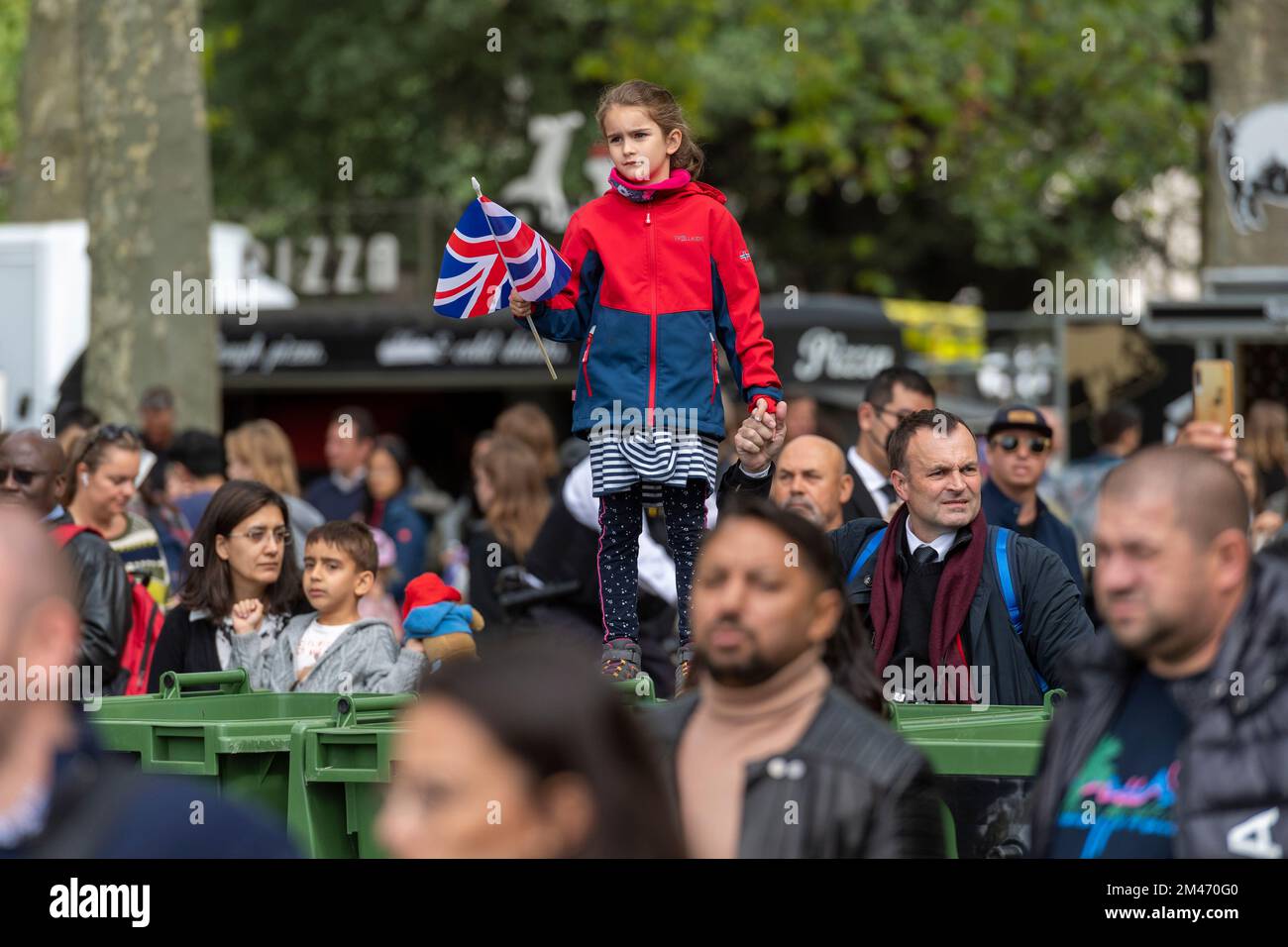A female child holding a Union Jack flag, in Hyde park, watching the live broadcast of the funeral Her Majesty Queen Elizabeth II taking place in West Stock Photo