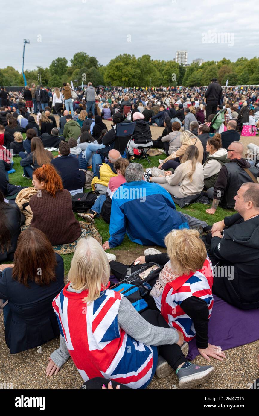 Two female mourner wearing a Union Jack jackets, in Hyde park watching the live broadcast of the funeral Her Majesty Queen Elizabeth II taking place i Stock Photo
