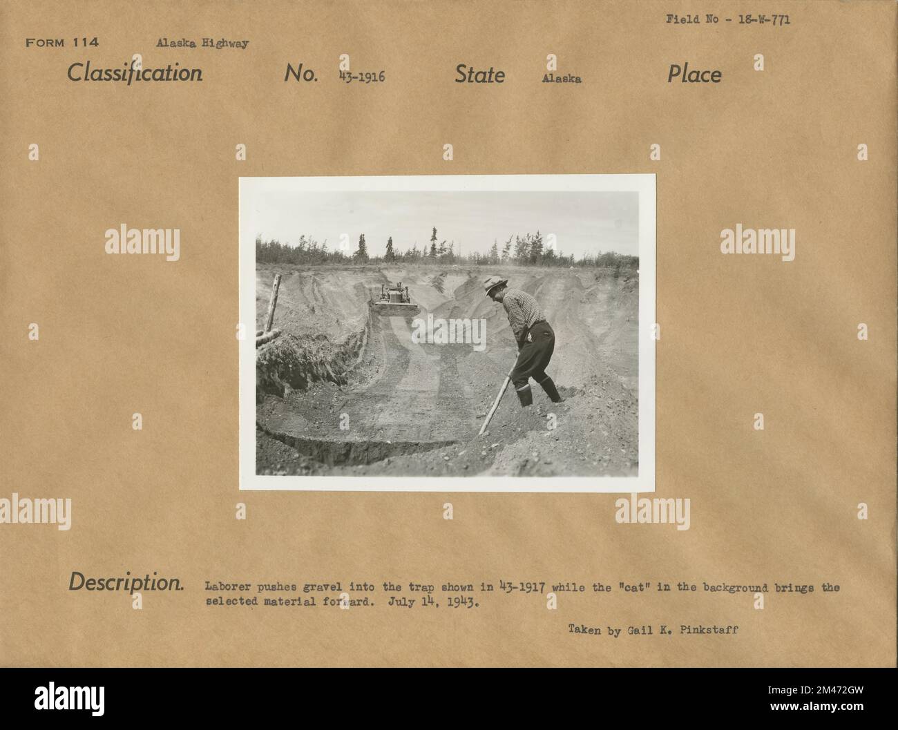 Laborer Pushes Gravel Into the Trap. Original caption: Laborer pushes gravel into the trap show in 43-1917 while the 'cat' in the background brings the selected material forward. Taken by Gail K. Pinkstaff. State: Alaska. Stock Photo