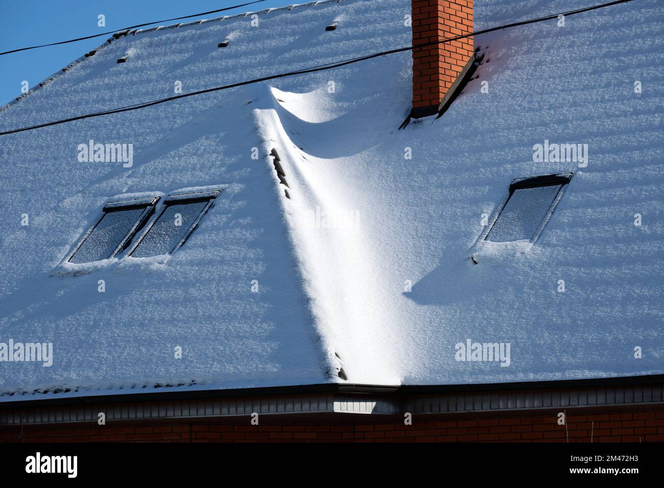 Closeup of house roof top with attic windows covered with snow in cold