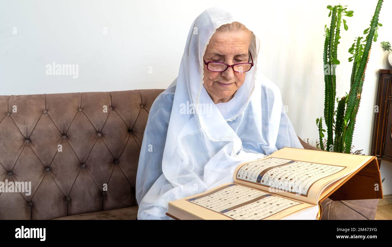Old Muslim woman reading the Holy Quran at home during Ramadan Month. Old woman wearing white hijab reading the Koran Stock Photo