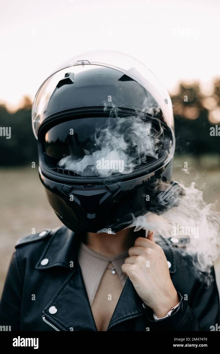 Biker girl puffs out smoke from under her helmet Stock Photo Alamy