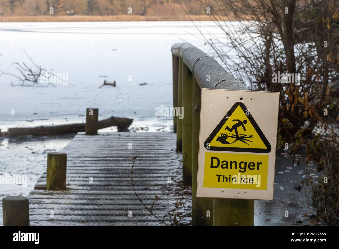 Danger Thin Ice warning signs beside a frozen lake, Fleet Pond, Hampshire, England, UK Stock Photo
