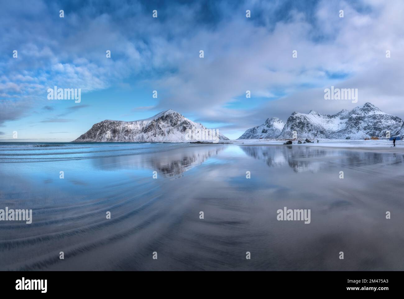 Sandy beach with blue sea reflected in water and rocks in snow Stock Photo