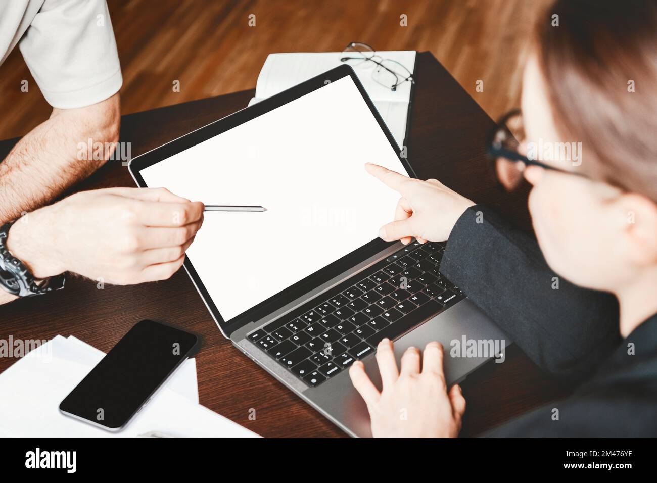 Blank screen of laptop on job desk in office and two business people pointing finger and pen at screen. Stock Photo