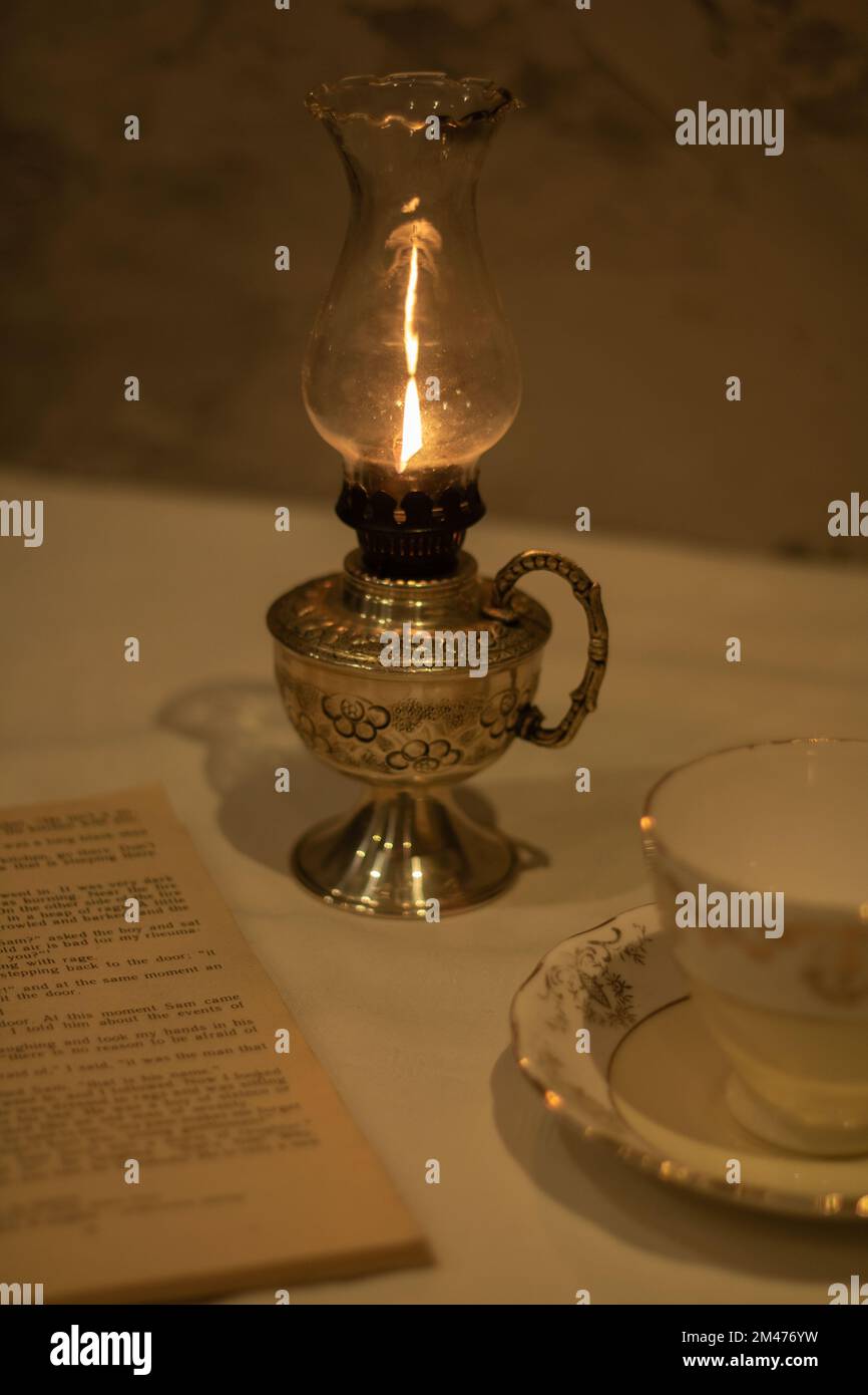 photo of a burning kerosene lamp, an old open book, an empty cup and