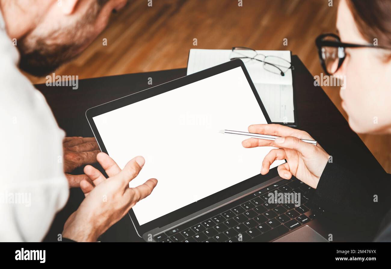 Two employees in office discussing business and pointing fingers at the screen of laptop. Stock Photo