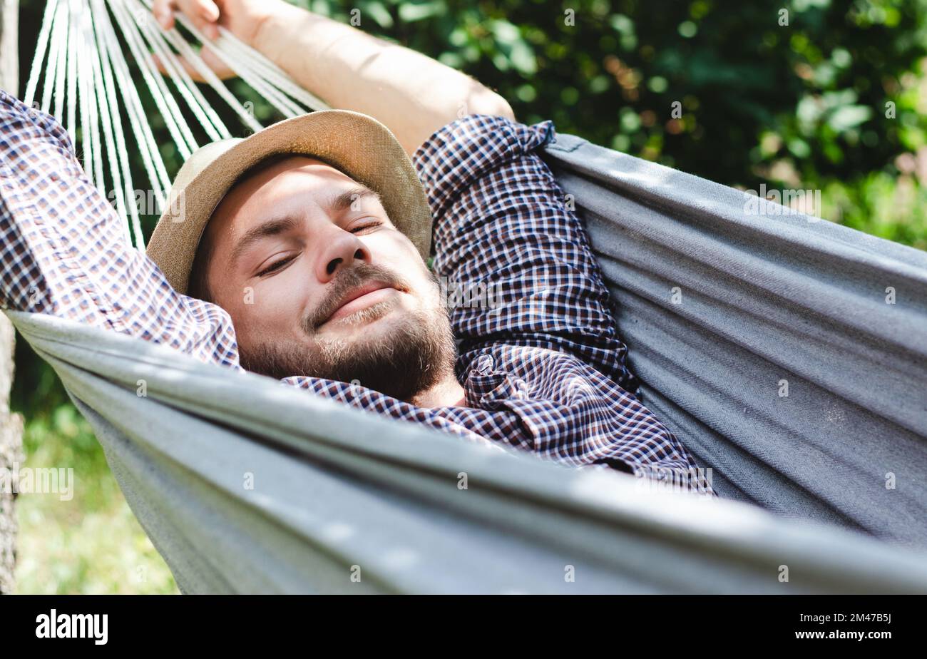 Bearded man in hat lying down on hammock. Stock Photo