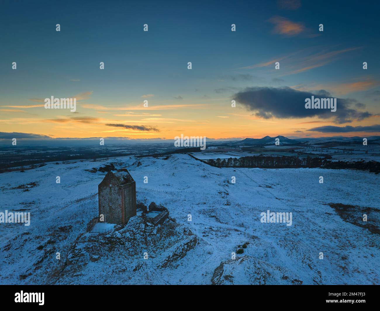 Aerial view of Smailholm Tower looking towards The Eildons at sunset on a crisp frosty winters day. Stock Photo