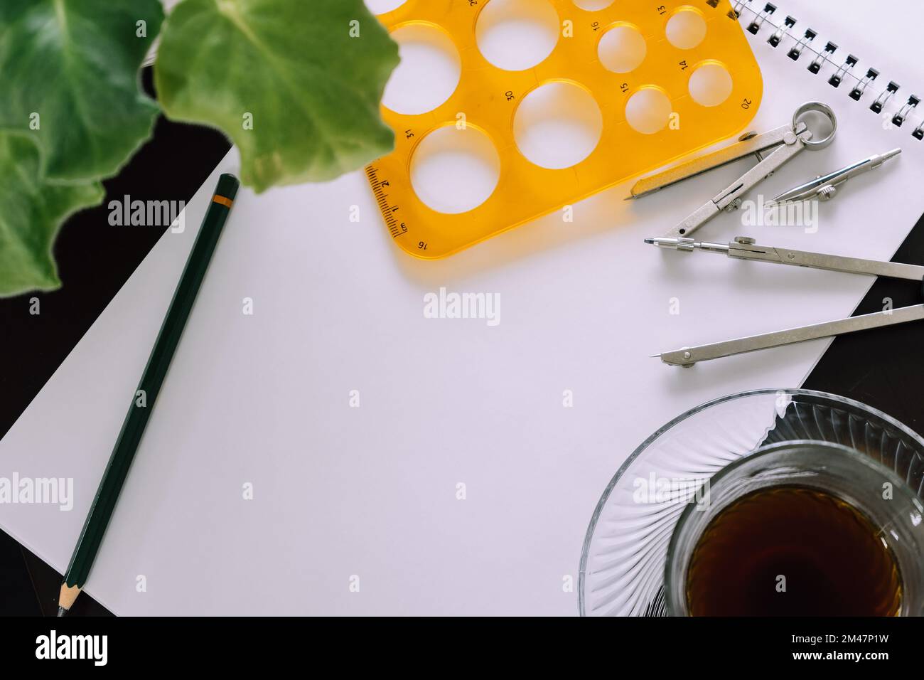 A top view of drawing materials, a green plant and a cup of tea on a black table Stock Photo