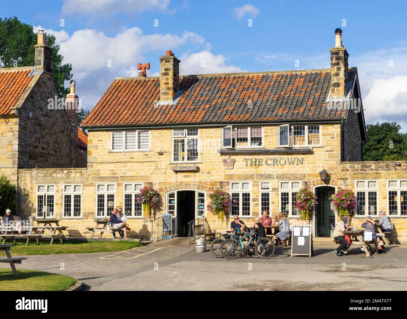 Hutton le Hole North Yorkshire People sat drinking outside The Crown pub on the green in Hutton le Hole Yorkshire UK GB Europe Stock Photo