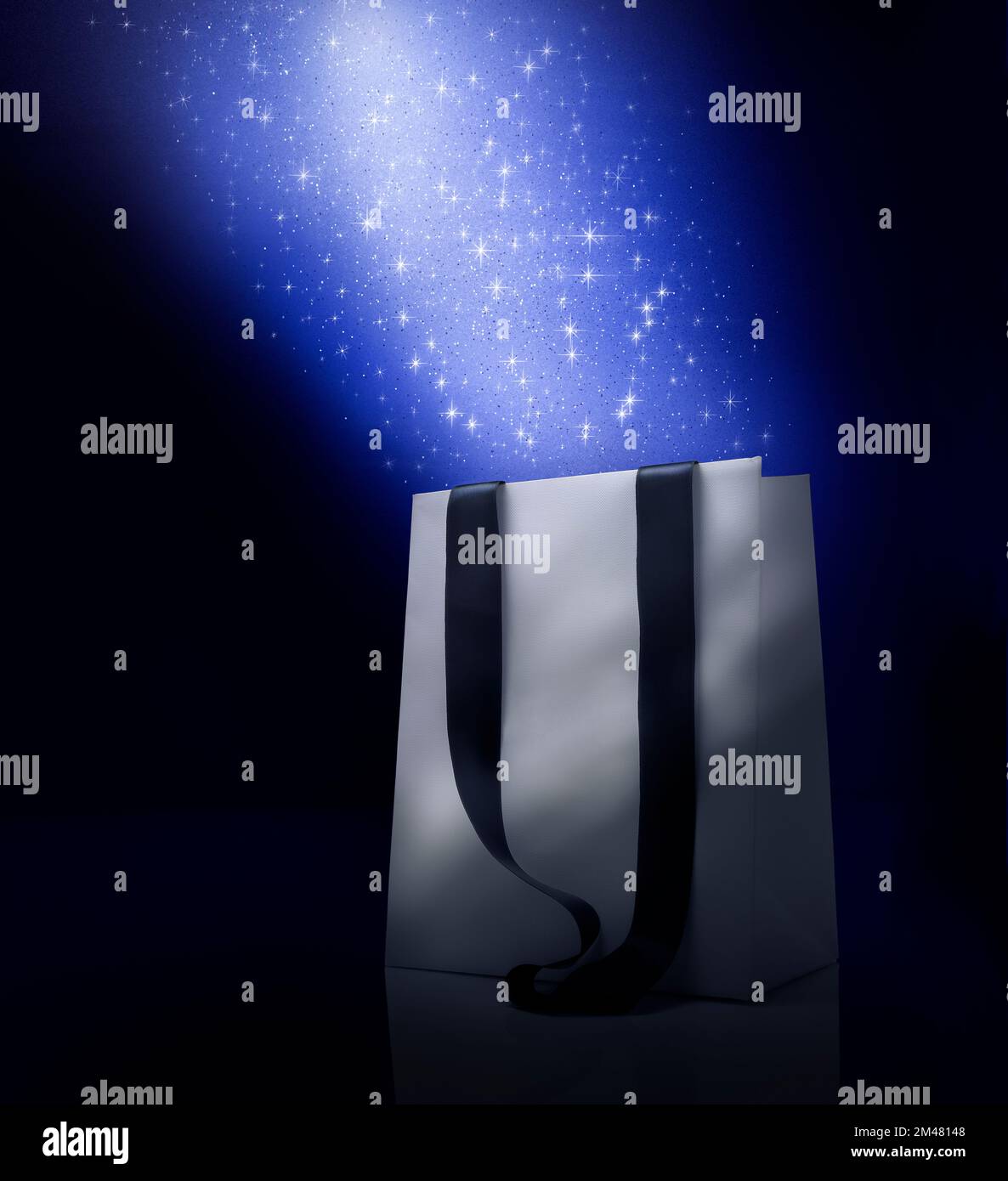 Fantasy Christmas shopping bag . Blue color stardust's effect over white bag. Black background and copy space Stock Photo