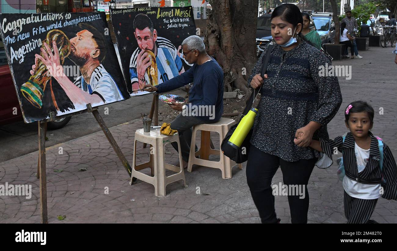 Mumbai, India. 19th Dec, 2022. A woman and a child walk by an artist from Gurukul school of art putting final touches to a painting of Lionel Messi kissing the World Cup trophy, the painting is a congratulation to Argentina on winning the football World Cup. Argentina won the FIFA (Federation Internationale de Football Association) world cup after 36 years since their last triumph over West Germany in 1986. (Photo by Ashish Vaishnav/SOPA Images/Sipa USA) Credit: Sipa USA/Alamy Live News Stock Photo