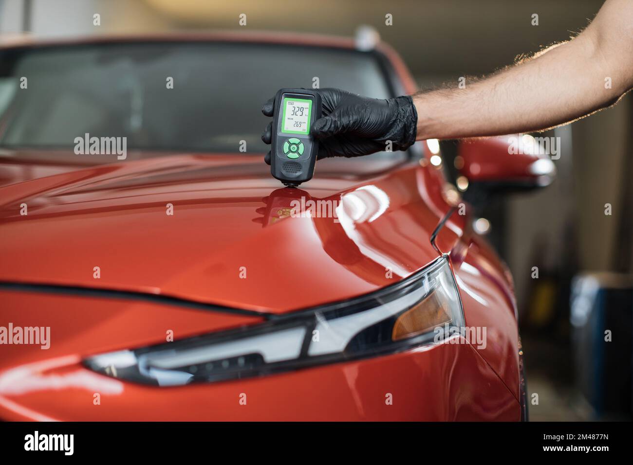 Inspector measuring paint cover thickness of red car body at the