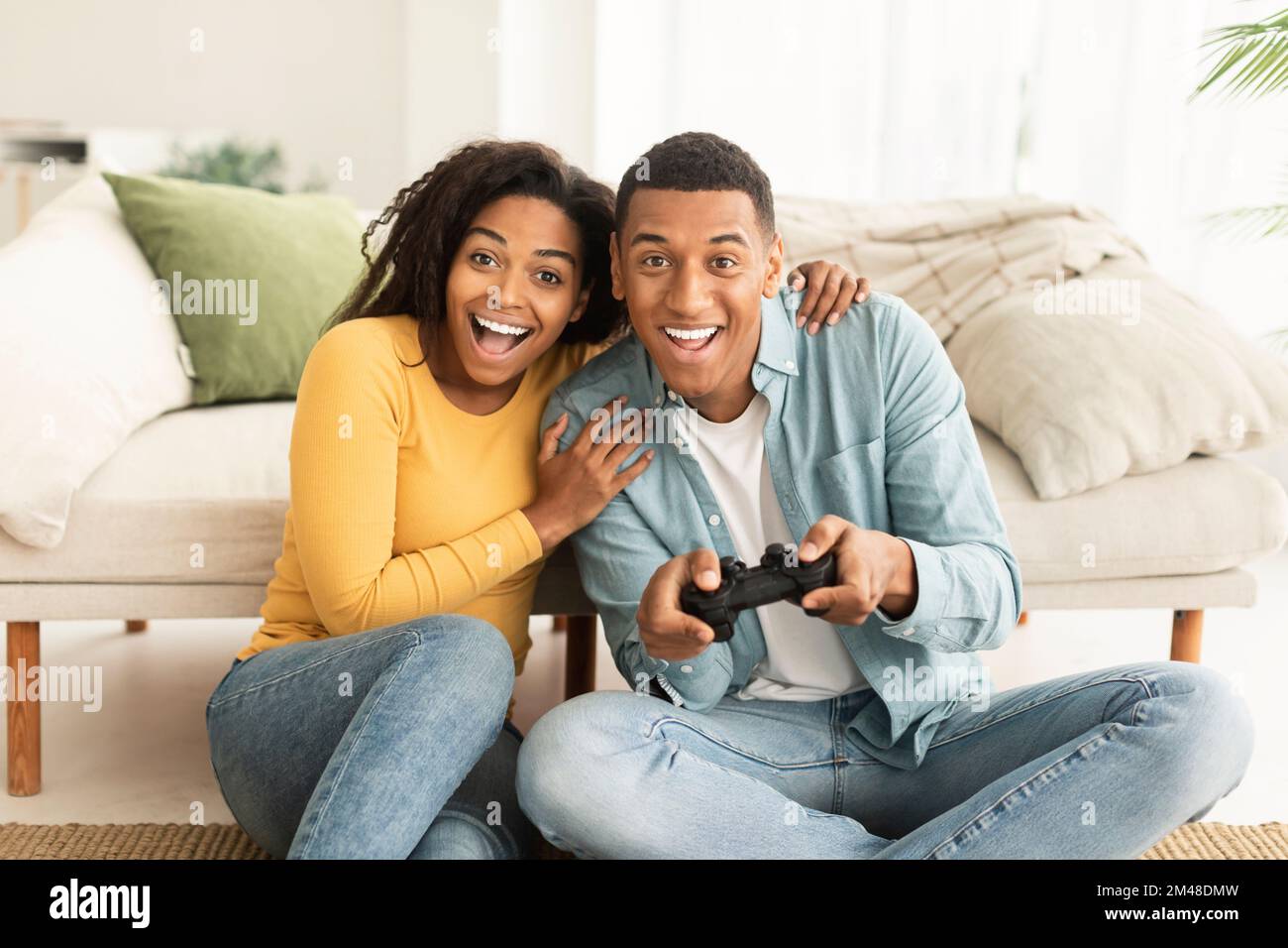 Happy excited young african american wife and husband sit on floor with ...