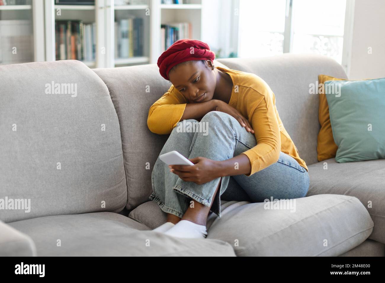 Stressed black woman sitting on sofa with cellphone Stock Photo