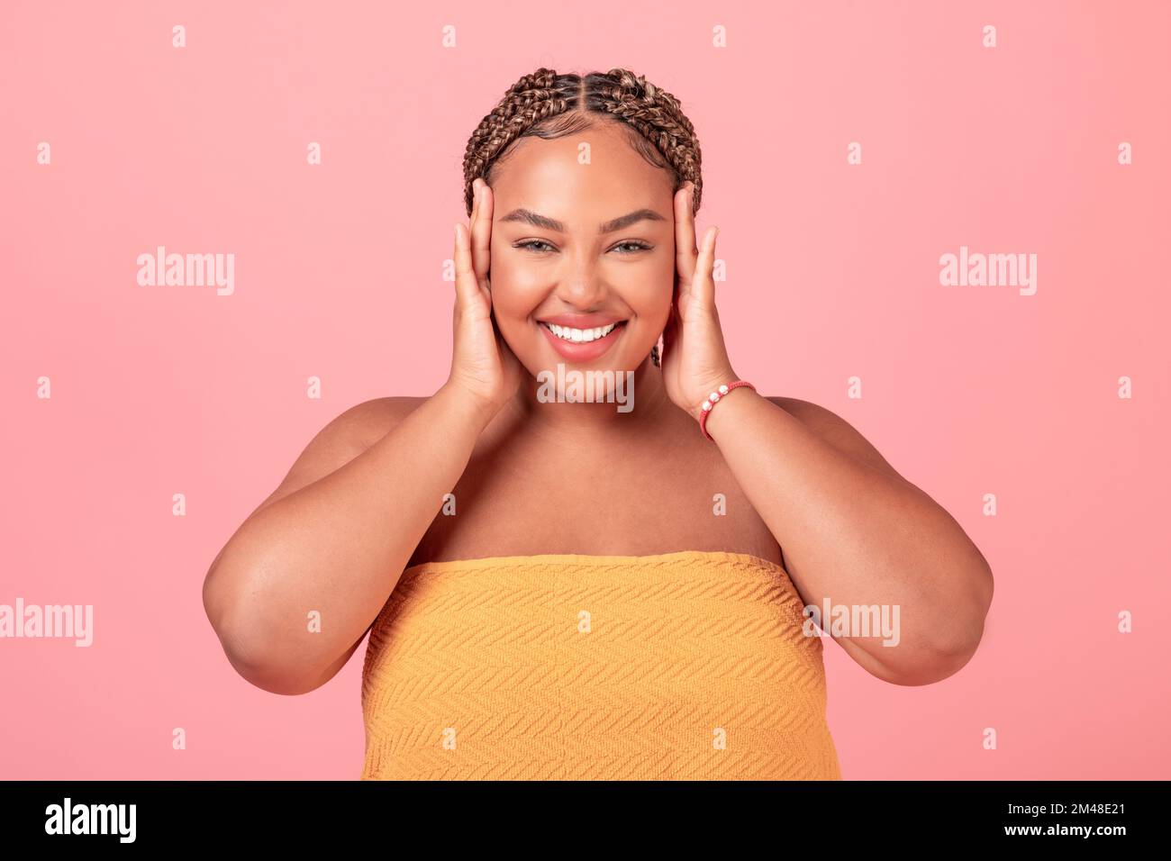 Portrait of excited black body positive woman touching face and enjoying her smooth skin, pink studio background Stock Photo