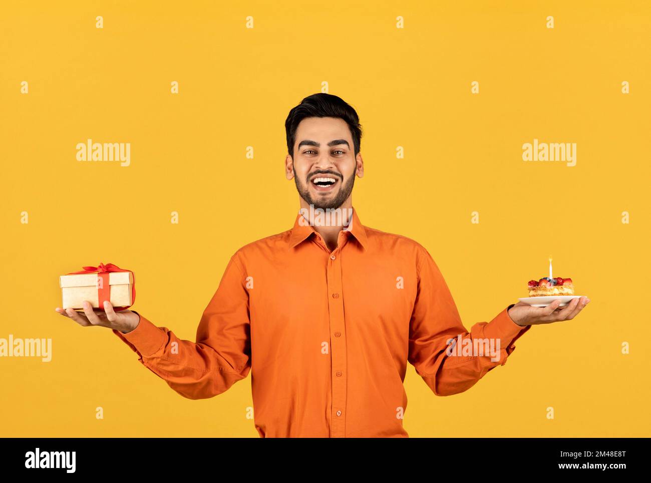 Happy Birthday. Joyful Arab Man Holding Gift Box And Cake With Candle Stock Photo