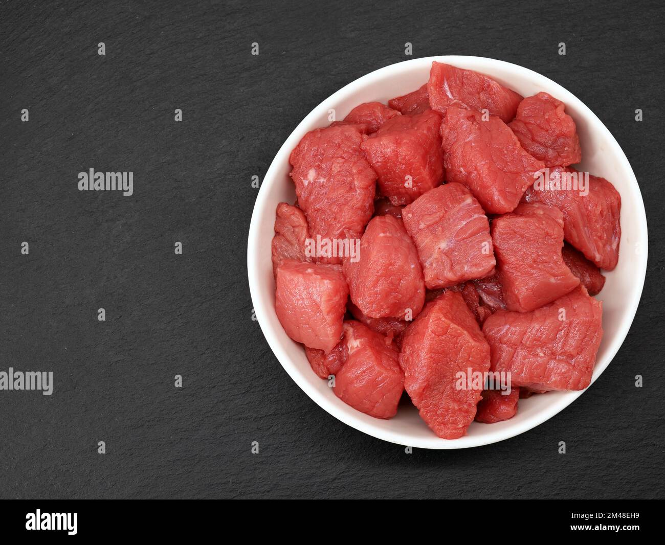 raw diced beef meat in white bowl on black slate background, top view Stock Photo