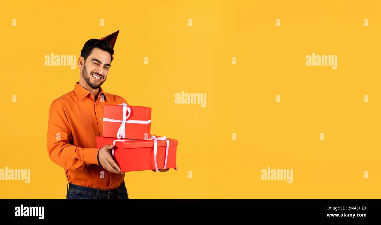 Happy Young Arab Man Holding Gift Boxes And Winking At Camera Stock Photo