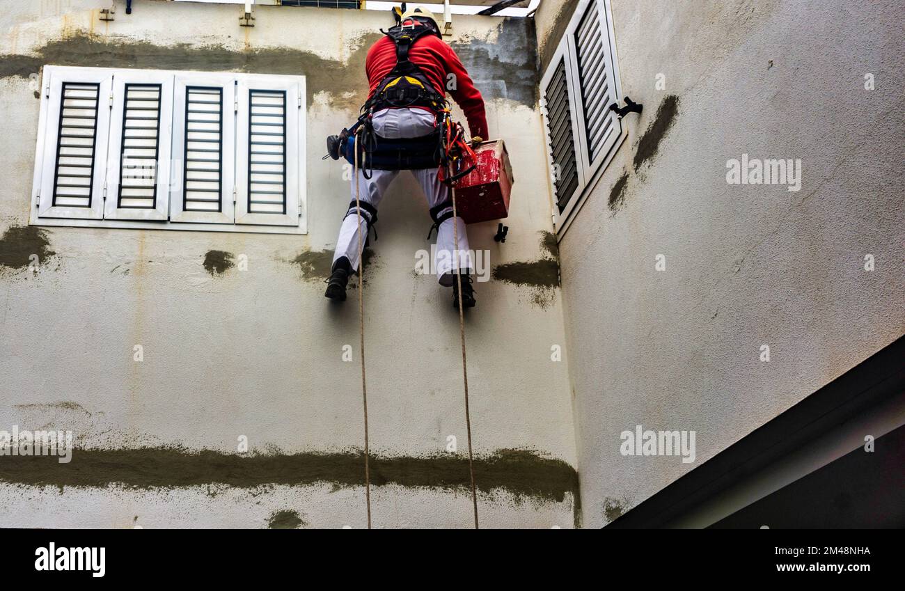A painter.decorator painting a high wall, while strapped into a safety