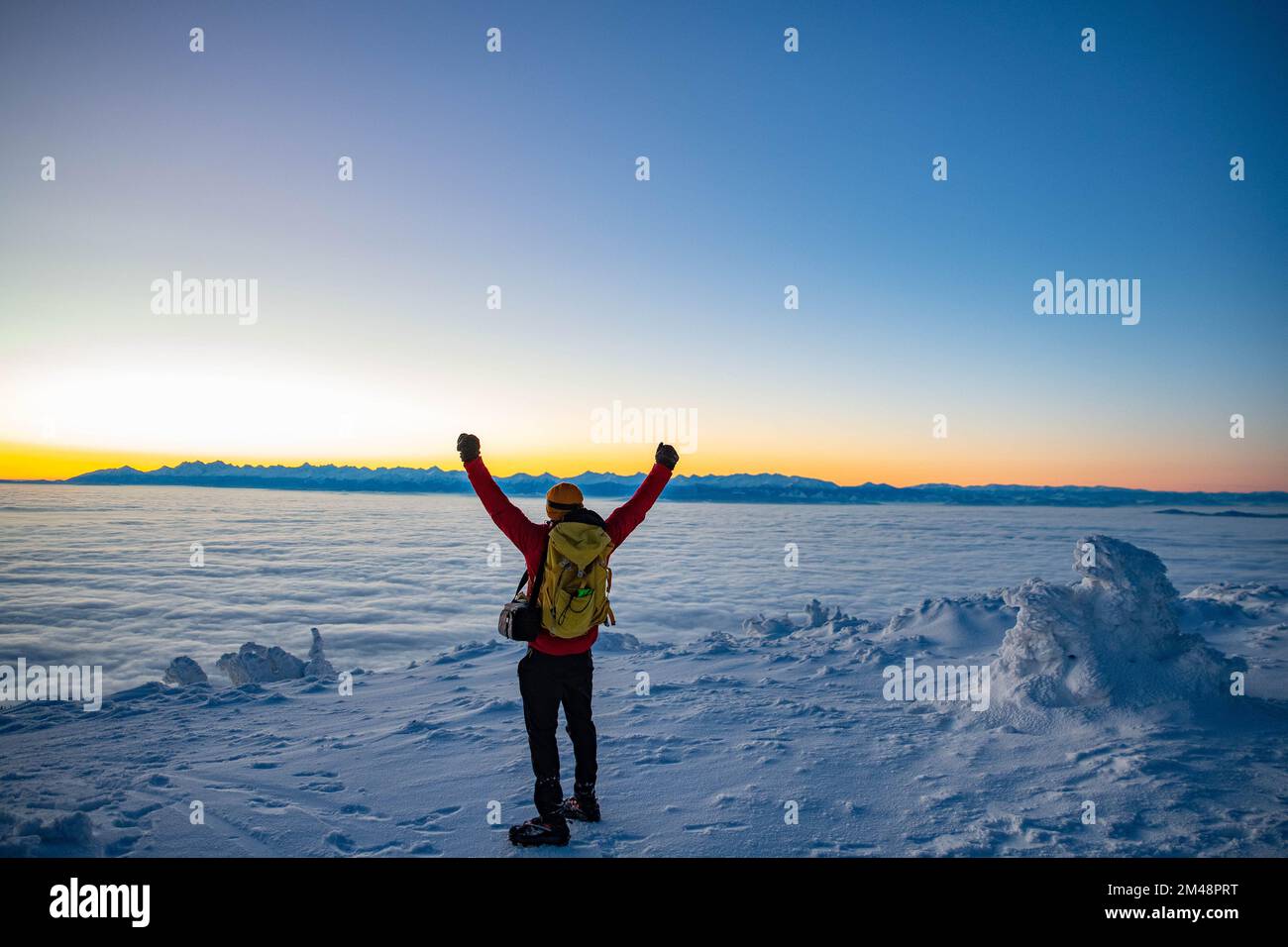 Man climbs a mountain peak in winter during sunrise. Sunrise on Babia Gora with a view to the Tatra Stock Photo