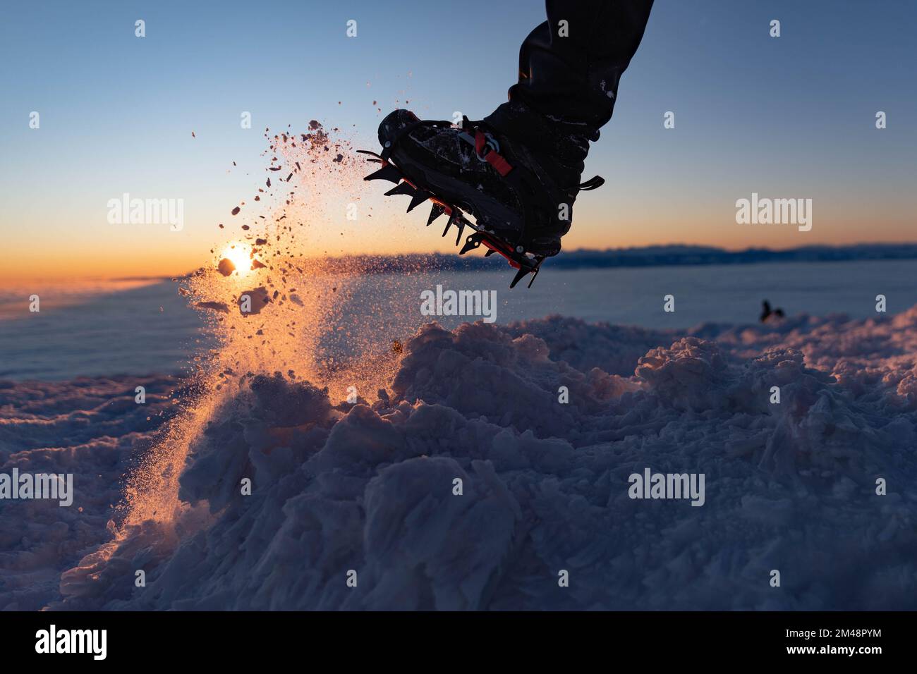 Man climbs a mountain peak in winter during sunrise. A shoe with spikes on - crampons.  Stock Photo
