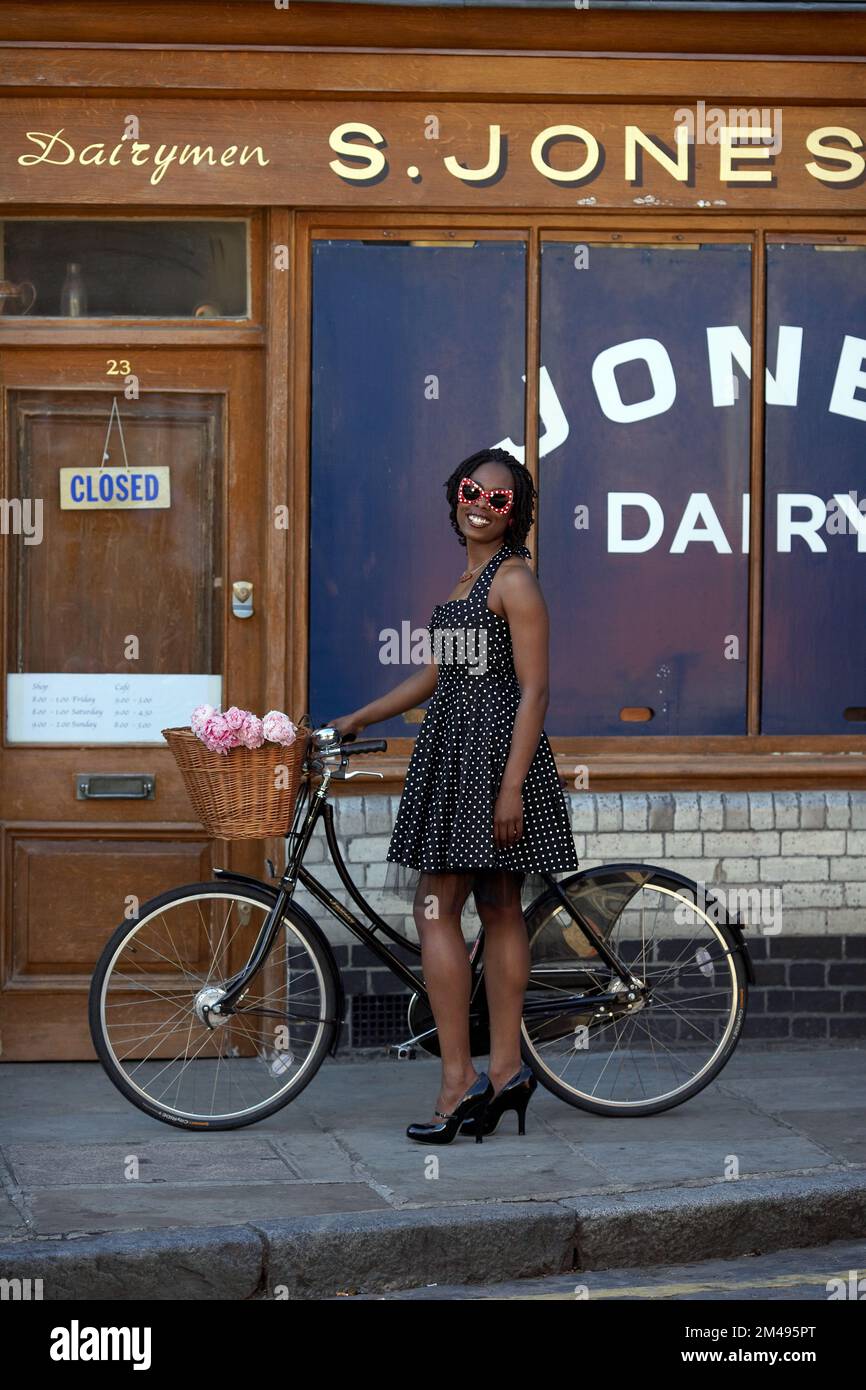 Girl standing with bicycle in front of vintage ,old shop front in Colombia Road ,Flower Market , East London , UK Stock Photo