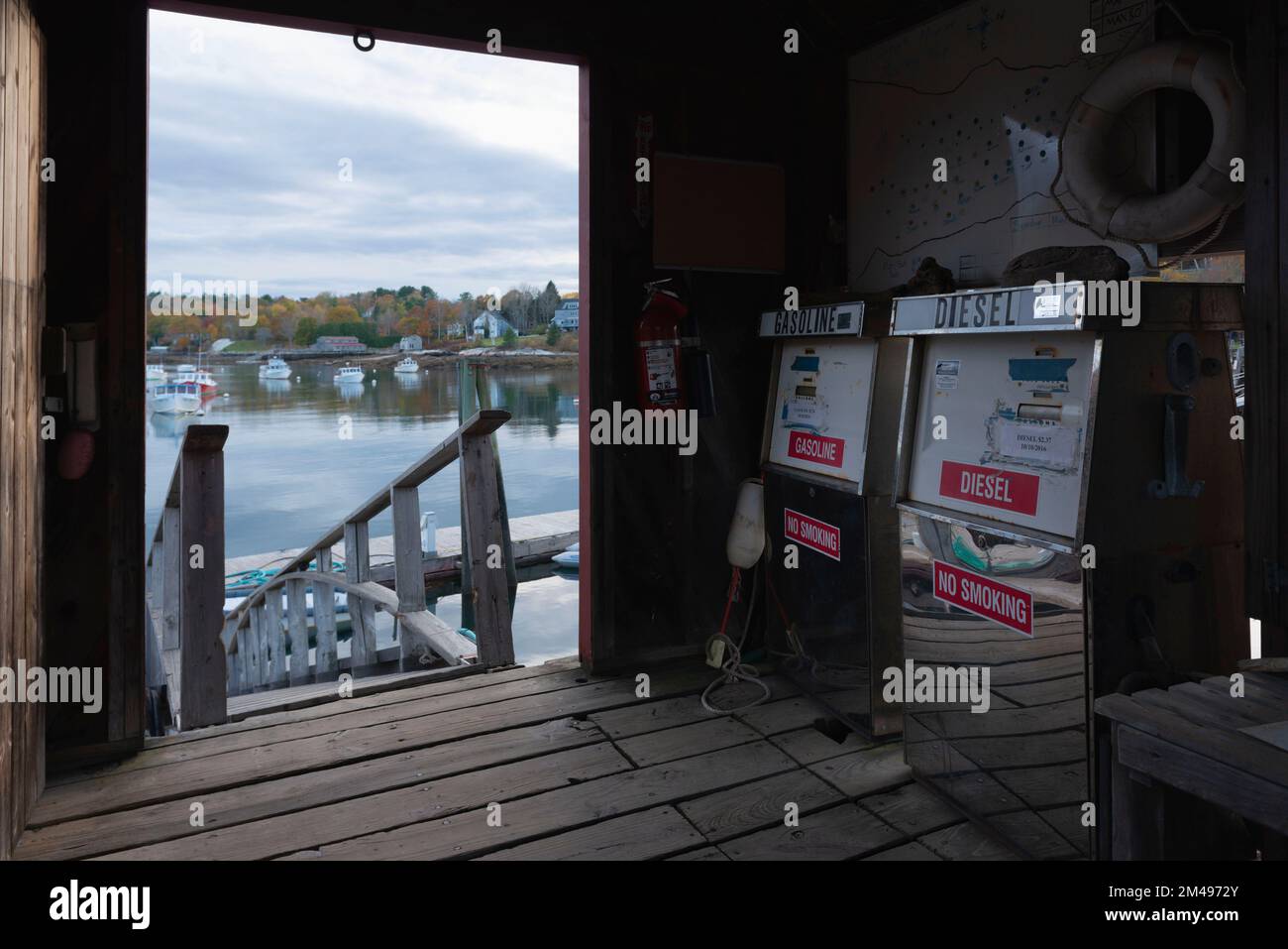 Fuel Pumps in a Wooden Shack on the Jetty at Rockport Marine on the Maine Coast, with a View Through the Doorway of the Moored Boats in the Bay Stock Photo